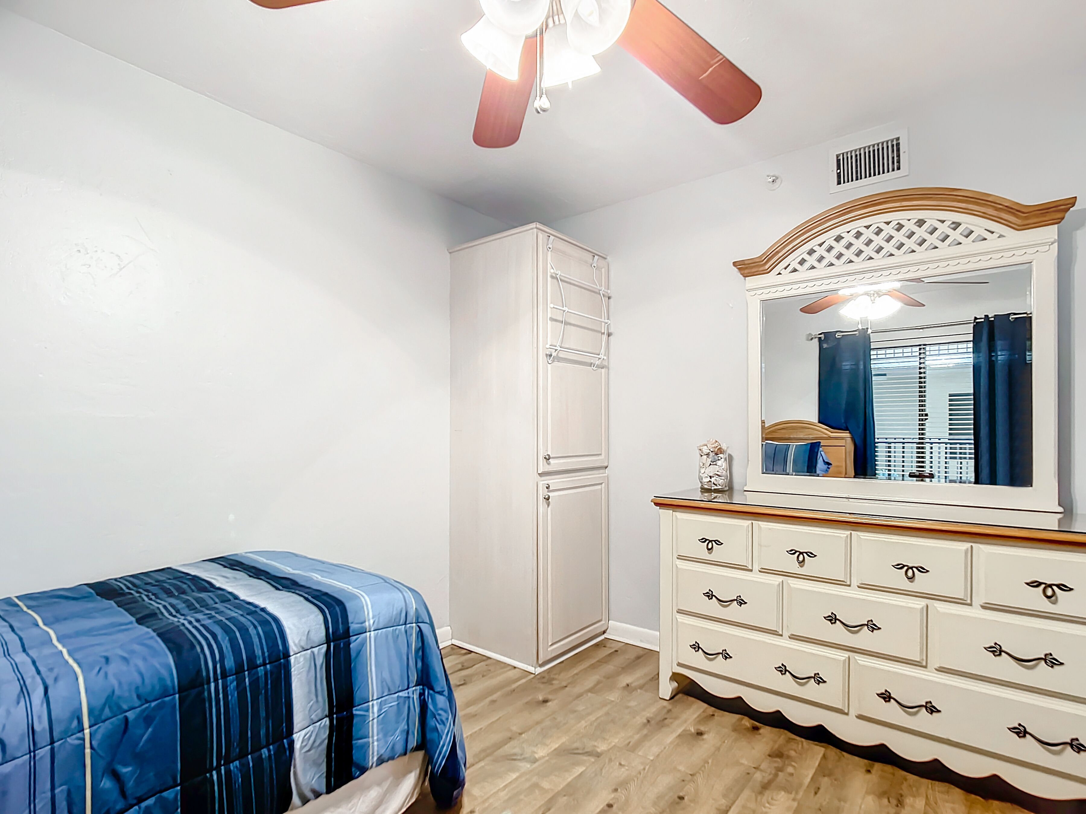 A bedroom with a bed, a dresser, a mirror, and a ceiling fan.