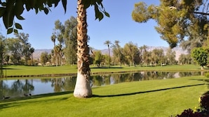 A well-maintained golf course with a pond, palm trees, and a clear view of distant mountains. - Fantastic Mt Views From this Beautiful Mission Hills Country Club Condo (Rancho Mirage)