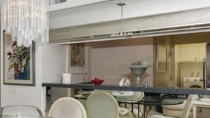 A modern kitchen with a glass dining table and wicker chairs, a chandelier, and a view into the adjacent living area. - Fantastic Mt Views From this Beautiful Mission Hills Country Club Condo (Rancho Mirage)
