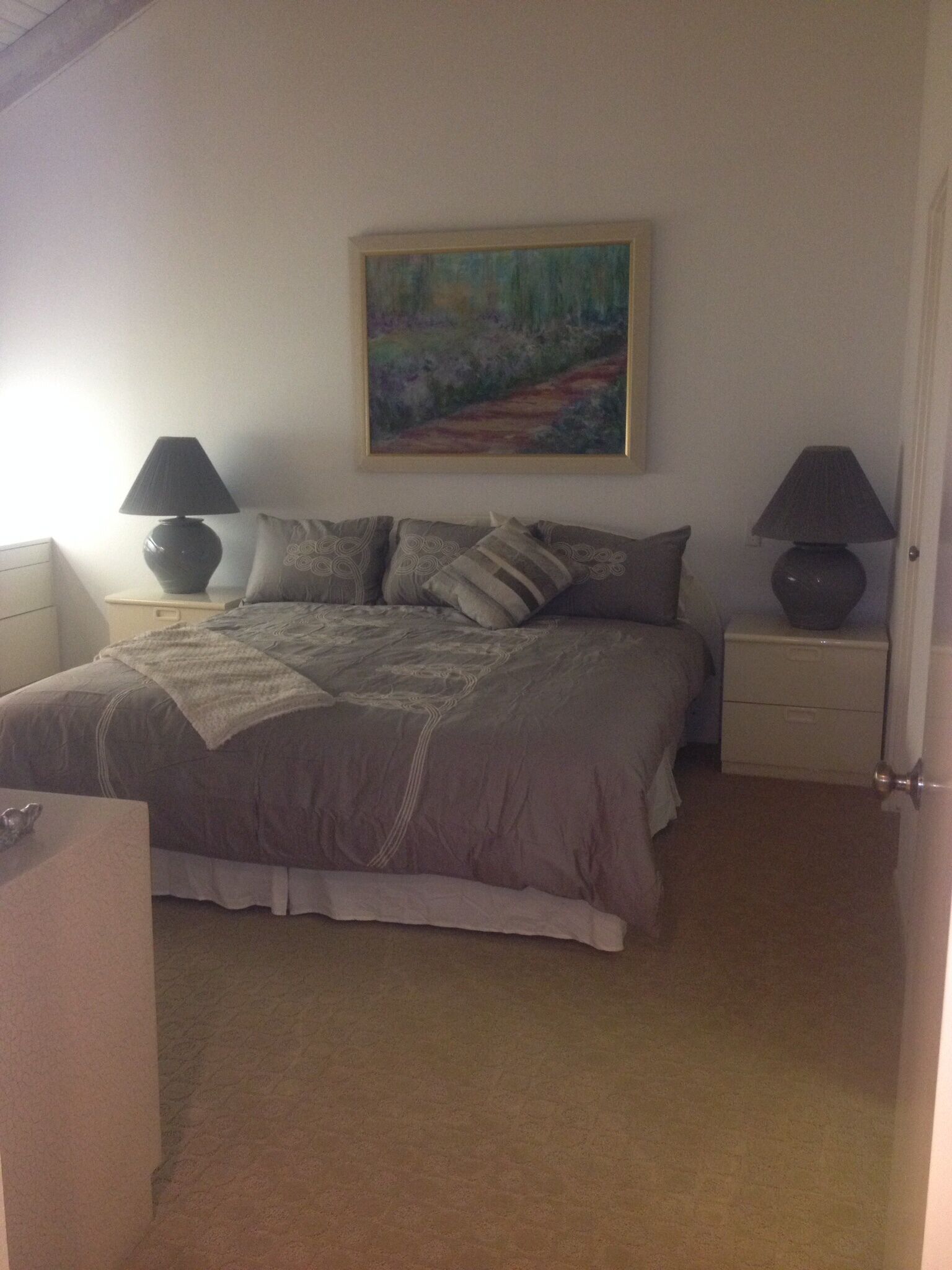 Un dormitorio con cama, dos mesitas de noche, un velador, un cuadro y una puerta.