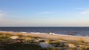A beach with a wooden boardwalk leading to the water, sandy dunes, and a clear sky.