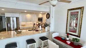 A modern kitchen with white cabinets, stainless steel appliances, and a bar area with stools.