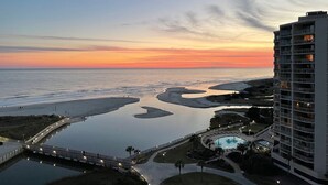 A high-rise hotel with a view of a beach and water at sunset.