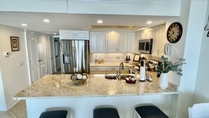 A modern kitchen with white cabinets, stainless steel appliances, a granite countertop, and three bar stools.