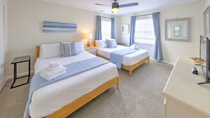A hotel room with two beds, a desk, a ceiling fan, and a large window with curtains.