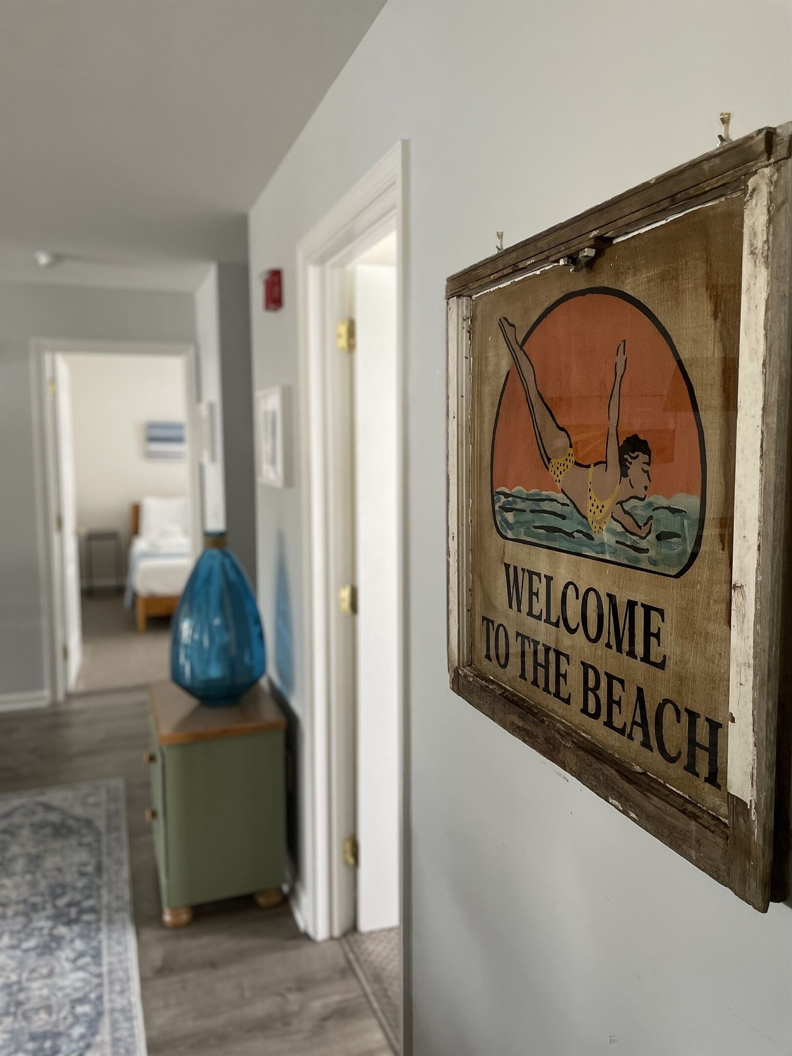 Ein Flur mit einem Schild, auf dem 'WELCOME TO THE BEACH' steht, und einer Tür im Vintage-Stil.