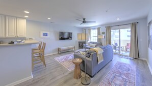 A modern living room with a grey sofa, wooden chairs, a small coffee table, and a TV mounted on the wall.
