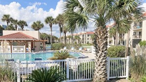 A pool area with white fences, palm trees, and a building with balconies in the background. - LOW RATES - Very Clean, Building G, 2/2 Pool, Beach, Tennis, Wifi Top floor (Saint Augustine)