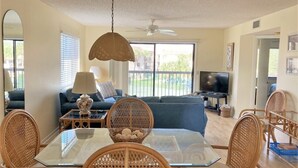 A dining area with a glass table and wicker chairs, a sofa in the background, and a ceiling fan. - LOW RATES - Very Clean, Building G, 2/2 Pool, Beach, Tennis, Wifi Top floor (Saint Augustine)