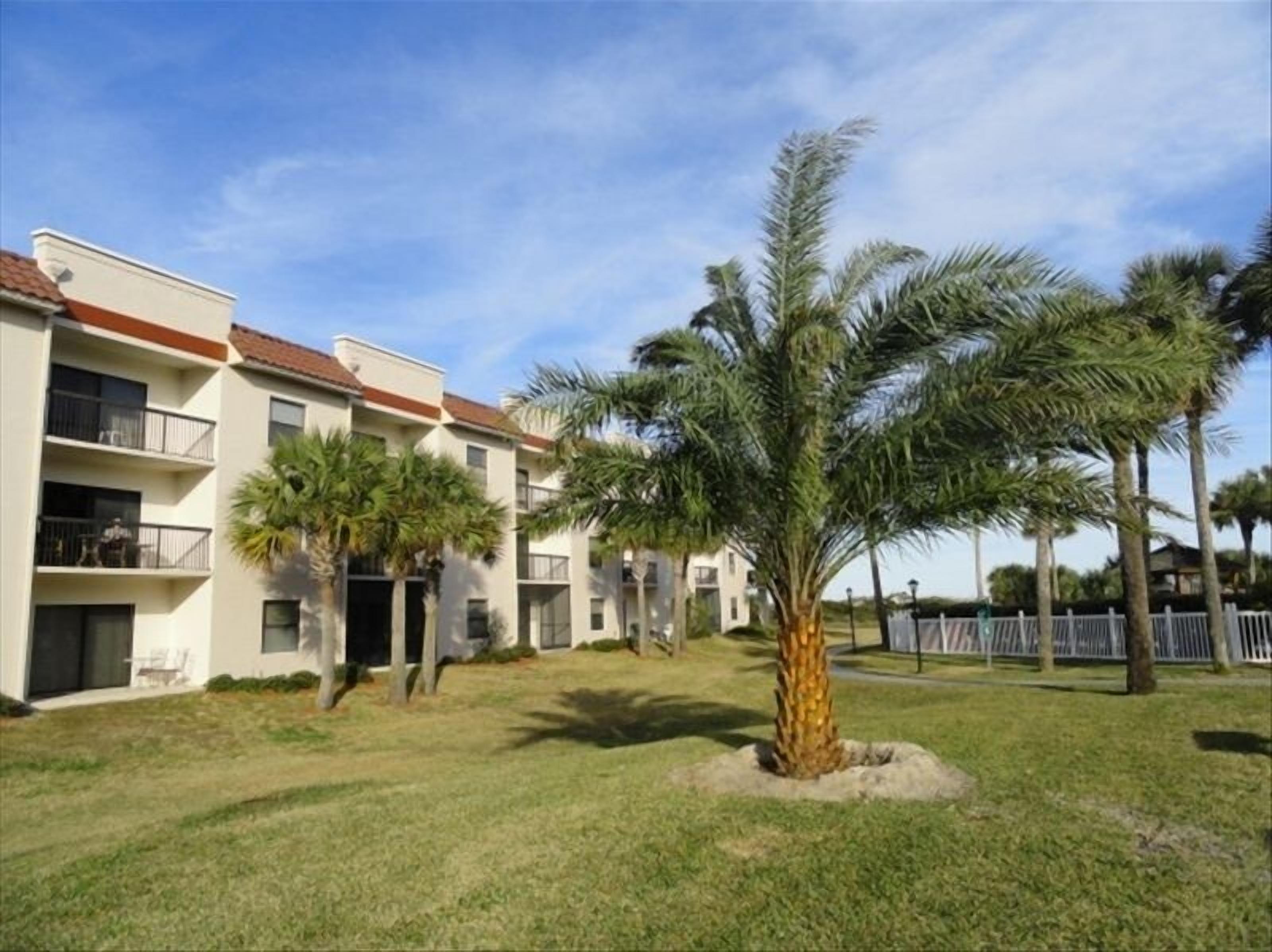 A multi-story building with balconies, surrounded by well-maintained grass and palm trees.