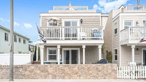 A two-story building with a balcony, a stone wall in front, and a sign indicating vacation rental availability.