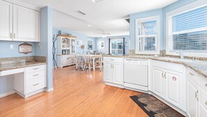 A spacious kitchen with white cabinetry, granite countertops, and a wooden dining area.