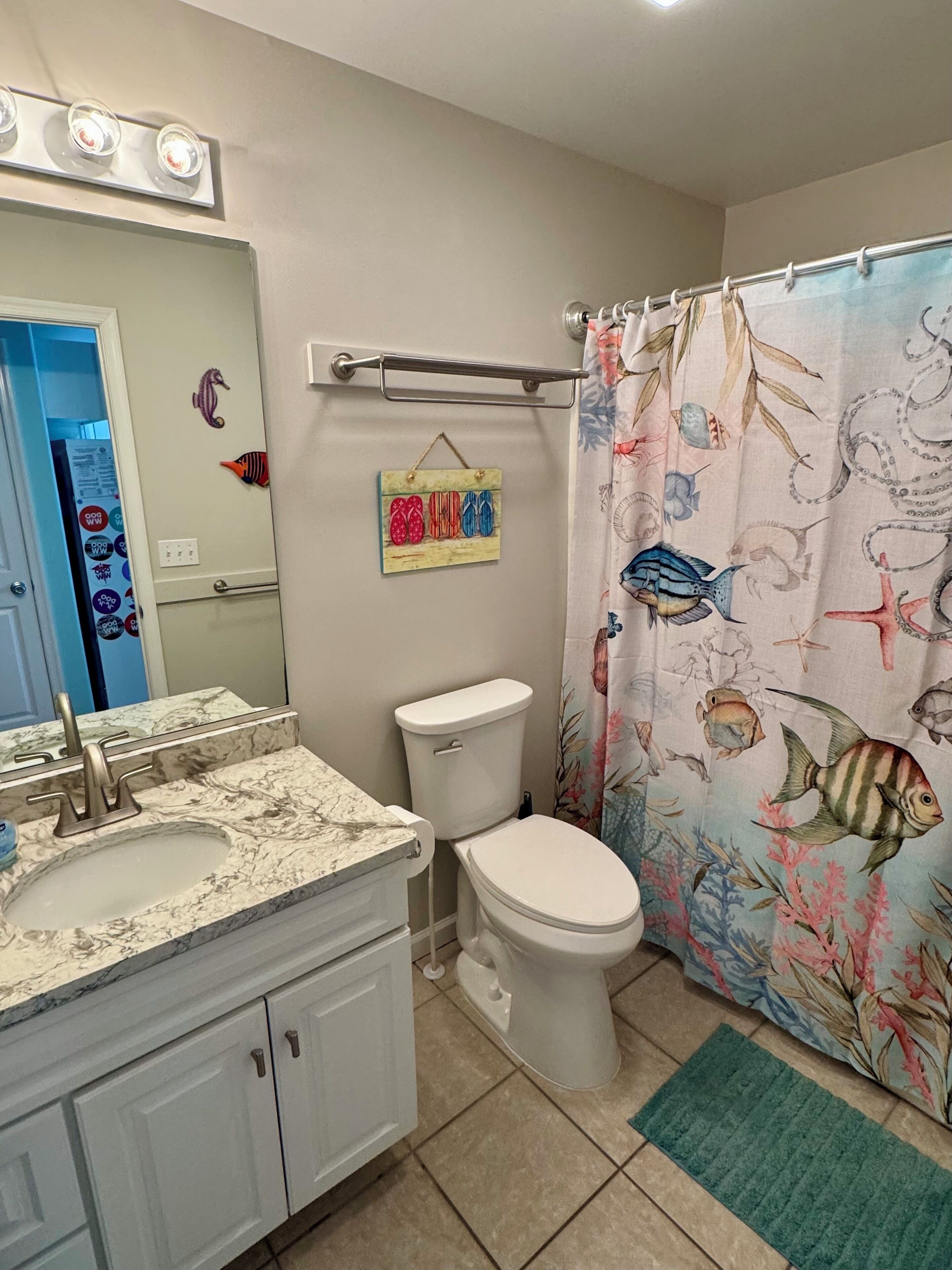 A bathroom with a marble sink, a toilet, and a shower curtain with a fish pattern.