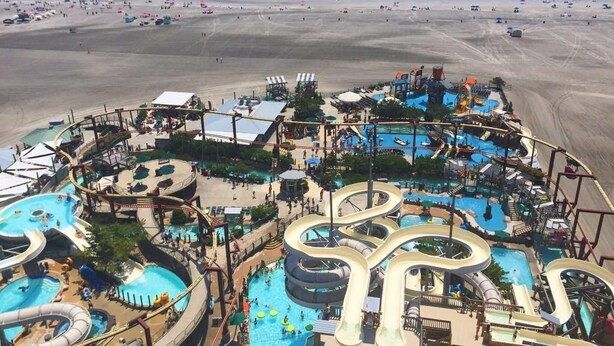 Een waterpark met verschillende glijbanen en zwembaden, omgeven door een zandstrand en de oceaan.