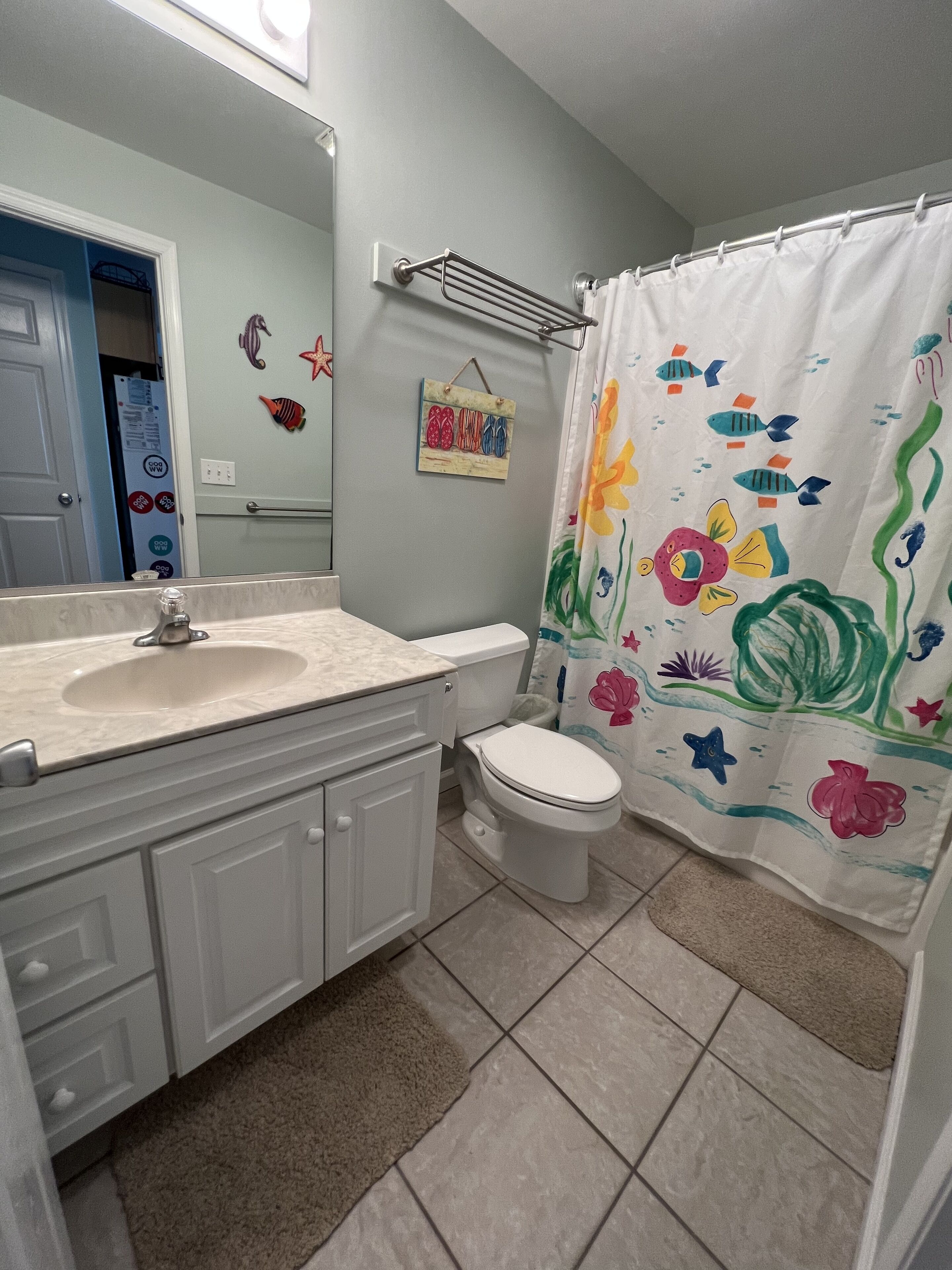 Une salle de bain avec un lavabo blanc, des toilettes et un rideau de douche orné de motifs de poissons.