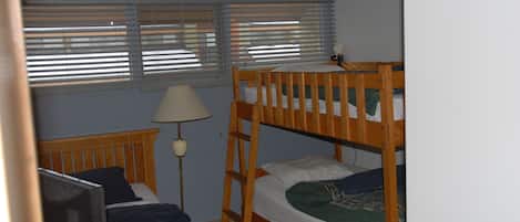 Quarto com beliche, televisão, luminária e janela com persianas.