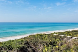 Une plage aux eaux turquoise et limpides, bordée d’un rivage sablonneux. Un sentier mène à la plage.