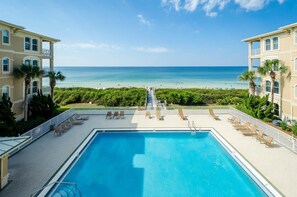 A pool area with a view of the ocean, surrounded by palm trees and a pathway leading to the beach.