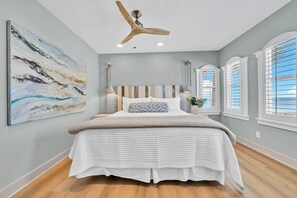 A bedroom with a large bed, a ceiling fan, and a painting on the wall.