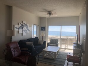 Relax in this stylish living room with a sofa, armchair, and wicker chair, offering a view of the beach.