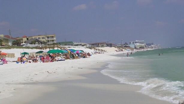 Ein Strand mit weißem Sand, Sonnenschirmen und Menschen.