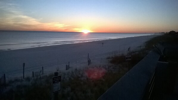 A beach with a sunset, a fence, and a sign.