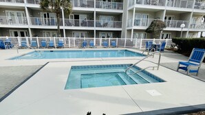 Ein Hotelpoolbereich mit mehreren Schwimmbecken, blauen Liegestühlen und einem weißen Zaun.