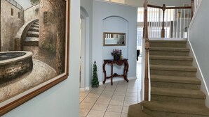 A hallway with a staircase, a framed painting, a mirror, and a small table with a plant. - S-Facing Pool, 3.6 mi from Disney, man-gated resort, wheelchair accessible (Kissimmee)