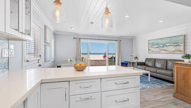 Una cocina moderna con armarios blancos, un comedor con vista a la playa y una sala de estar con sofá de cuero.
