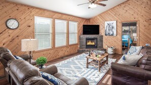 Ein gemütliches Wohnzimmer mit Kamin, Ledersofas, Fernseher und Holzwänden.