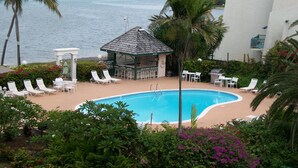 A pool area with lounge chairs, a small gazebo, and a view of the sea. - Beach Condo in Great Location with Cruzan Rum Bar (Christiansted)