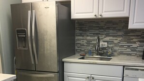 A compact kitchen with white cabinets, a stainless steel refrigerator, a tiled backsplash, and a small countertop. - Beach Condo in Great Location with Cruzan Rum Bar (Christiansted)