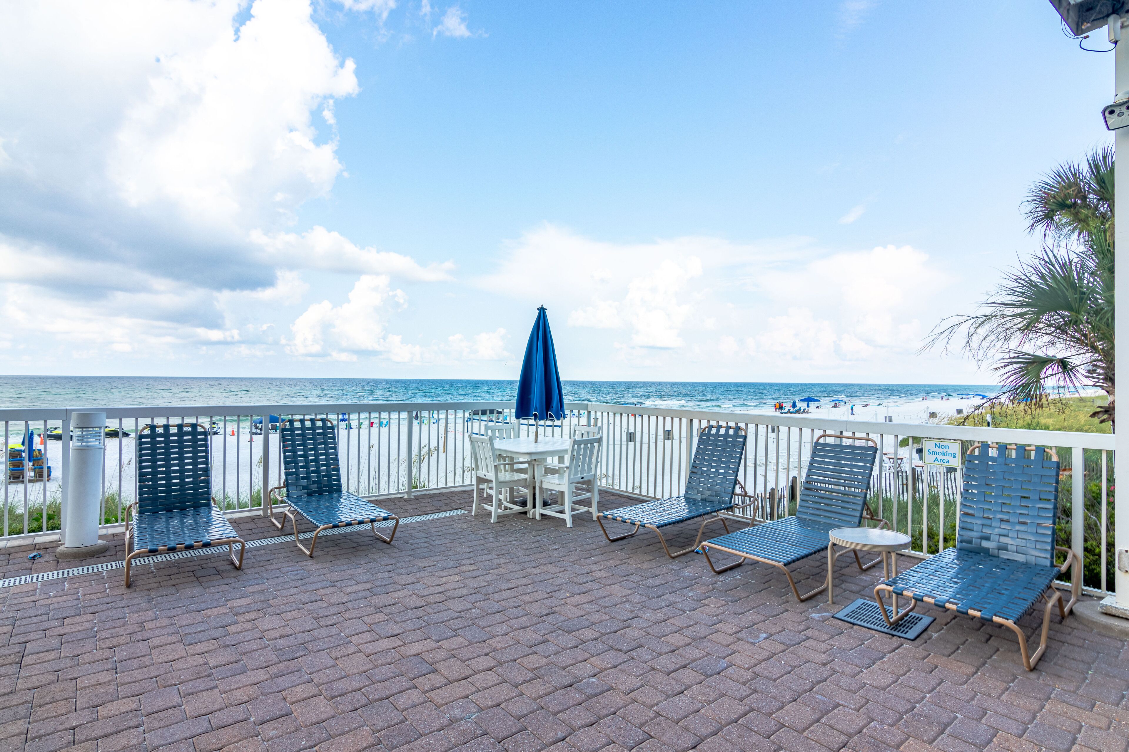 A patio with a table and chairs, a blue umbrella, and a view of the ocean.