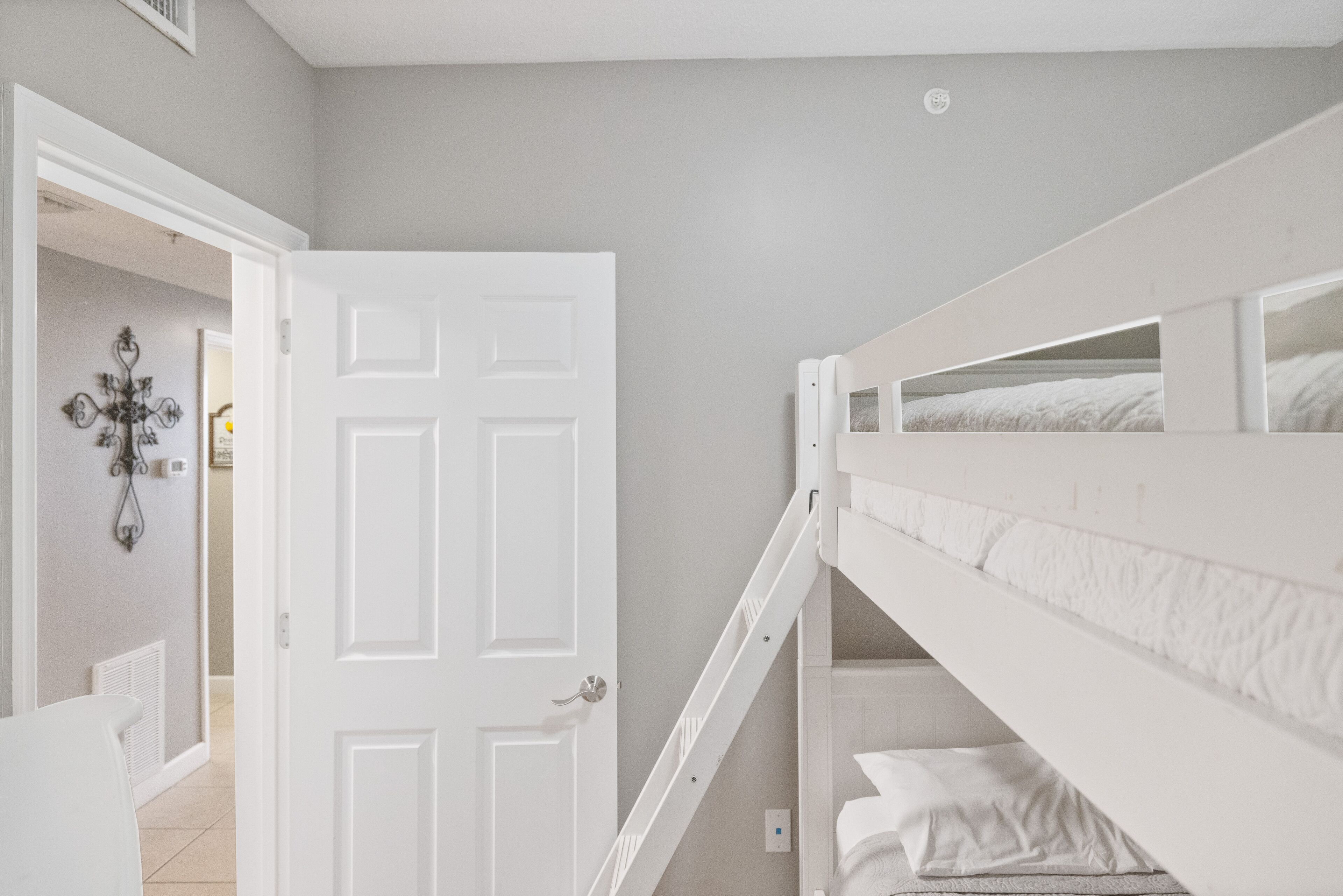 Quarto com uma cama de solteiro e beliche, uma porta branca e uma janela pequena.