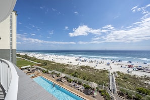 A poolside view with a beach and ocean in the background.