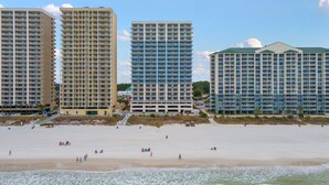 Ein Strandhotel mit mehreren Hochhäusern, einem Sandstrand und Meereswellen.