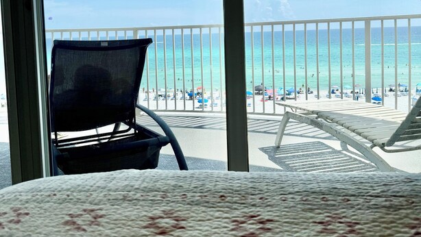Ein Balkon mit Blick auf einen Strand, ein Stuhl und ein Bett mit gemustertem Überwurf.