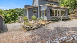 A two-story house with a covered porch, a stone retaining wall, and a gravel driveway. - The Big Blue House - 6000sf of Luxury in Leiper's Fork (Franklin)
