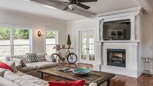 A spacious living room with a fireplace, a large TV mounted above it, and a bicycle in the corner. - The Big Blue House - 6000sf of Luxury in Leiper's Fork (Franklin)