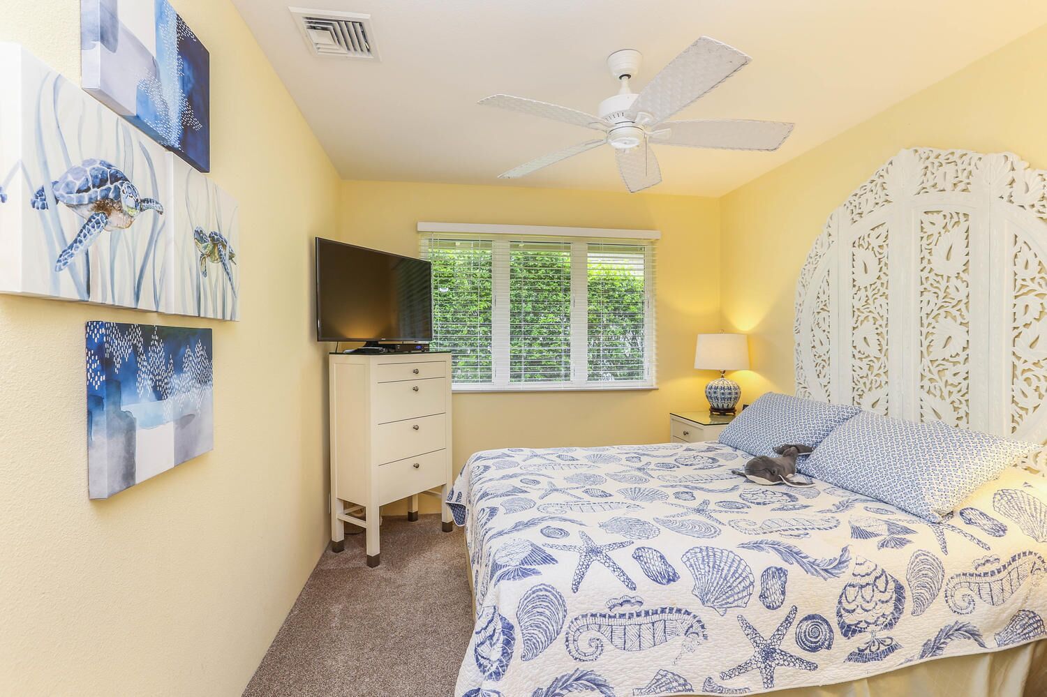 A bedroom with a bed, a TV, a window, and artwork on the wall.