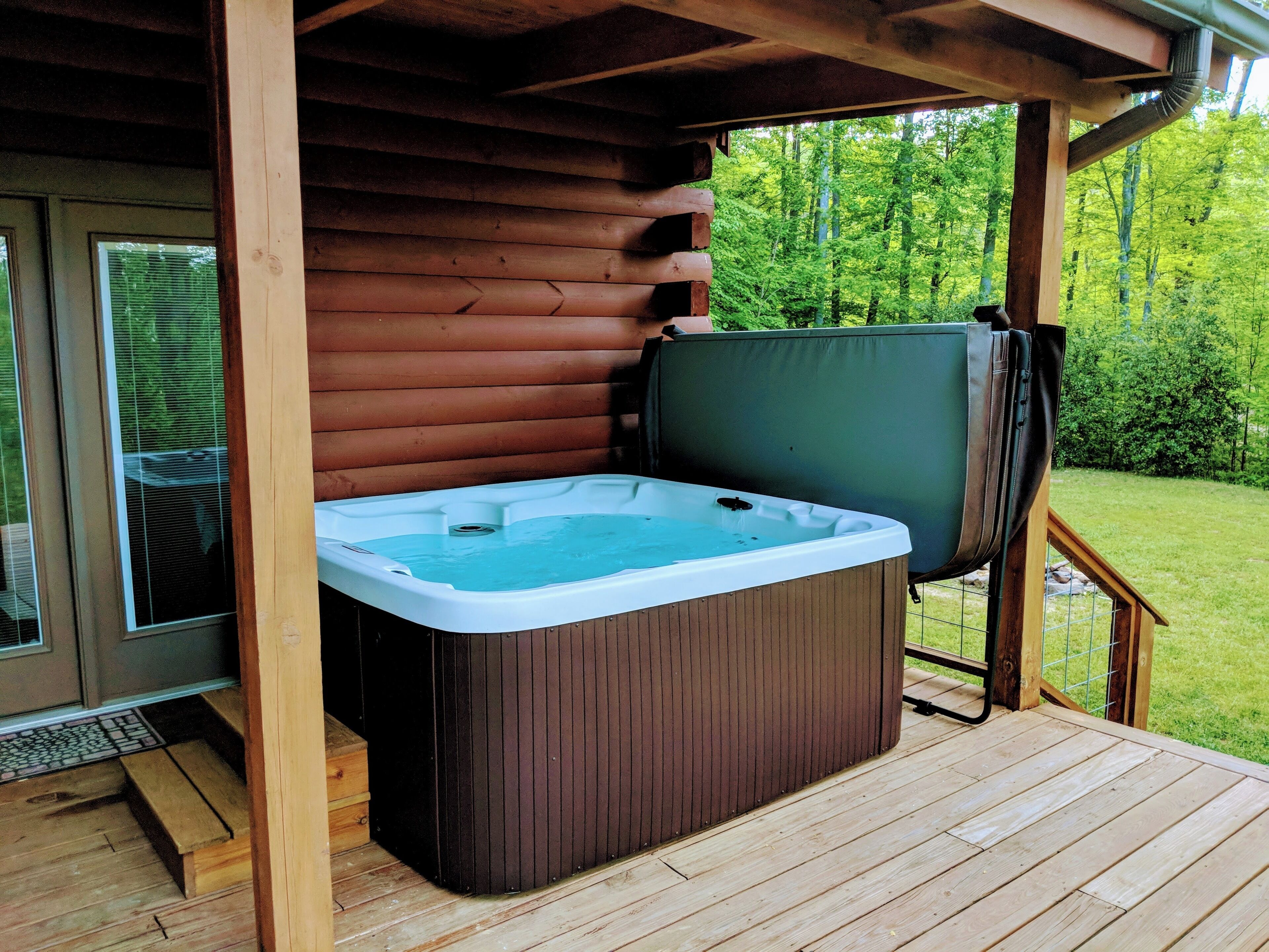 Ein Whirlpool auf einer Holzterrasse mit Blick auf einen Wald.