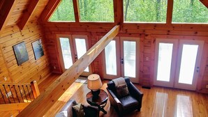A spacious loft with a high ceiling, wooden beams, a large window, and a cozy seating area with leather sofas and a coffee table.