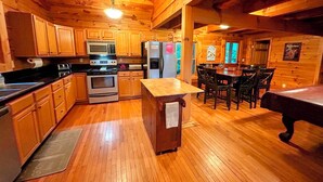 A wooden cabin interior with a kitchen featuring wooden cabinets, a microwave, stove, refrigerator, and a dining area with a table and chairs.