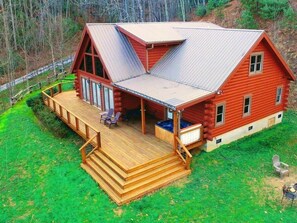 Eine rote Blockhütte mit einer Holzterrasse und einem Whirlpool.