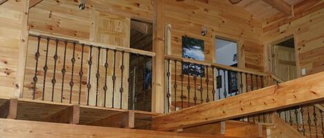 L’intérieur d’un chalet en bois, avec un escalier en bois, un ventilateur de plafond et une fenêtre offrant une vue.