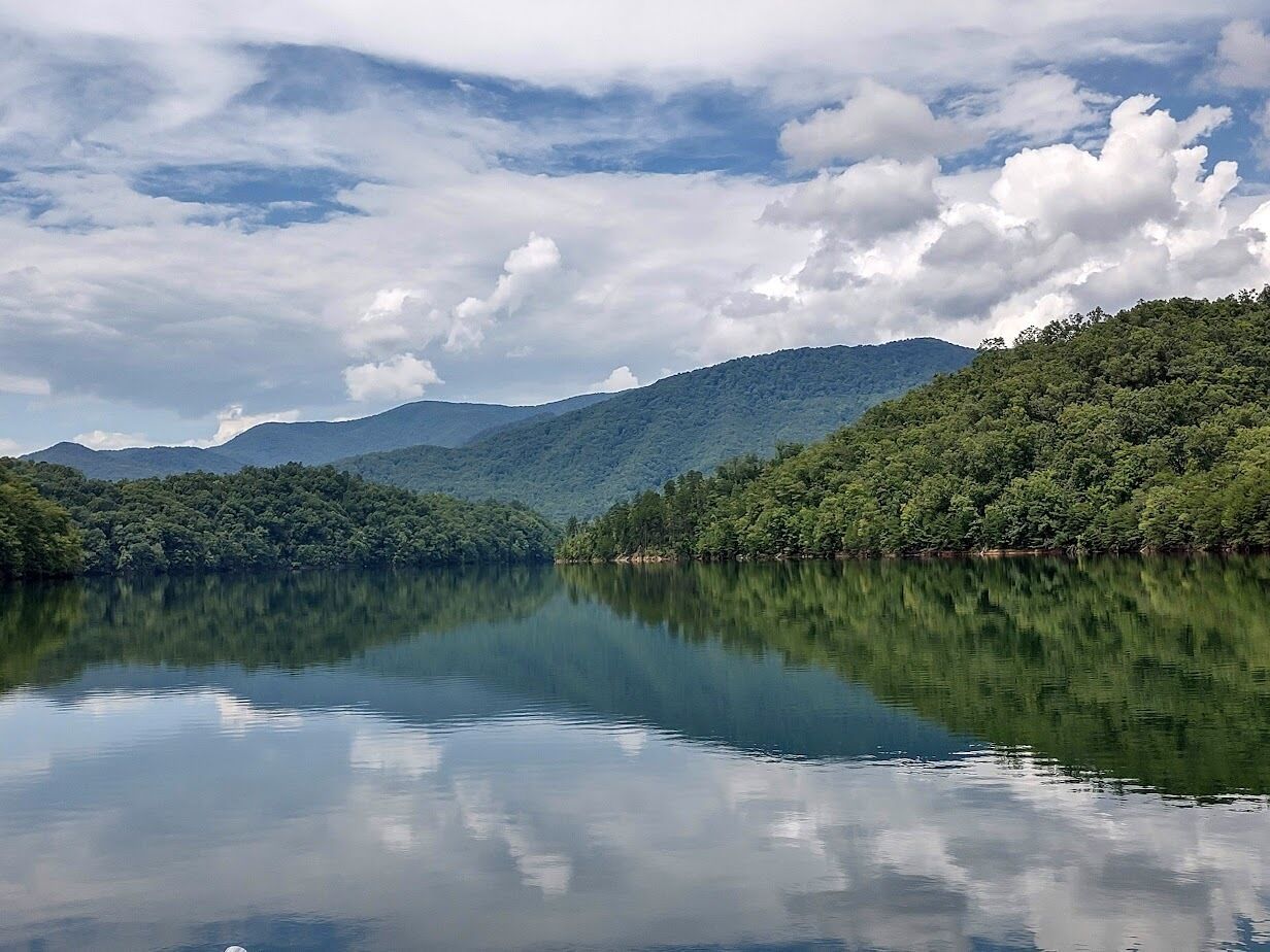 A calm lake with a mountain backdrop and dense forest.