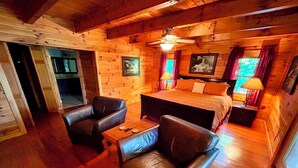 A cozy log cabin room with a bed, two leather chairs, a small table, and wooden walls.