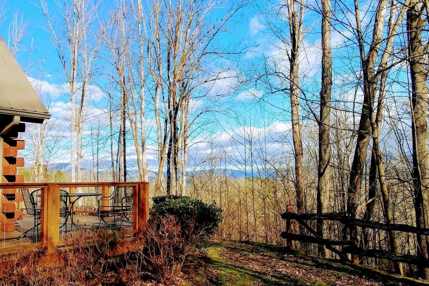 A cabin with a deck, surrounded by a forest and a clear sky.