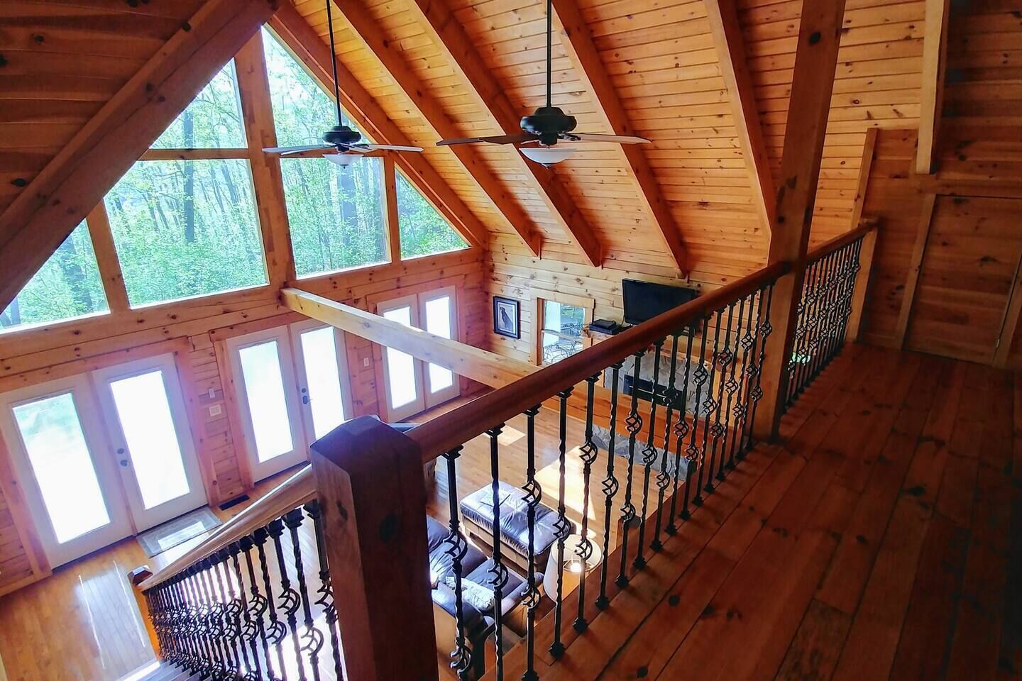 A wooden cabin with a loft bedroom, a balcony, and a view of the forest.