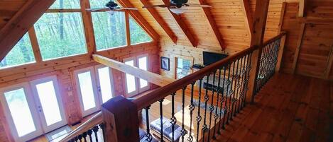 A wooden cabin with a loft bedroom, a balcony, and a view of the forest.